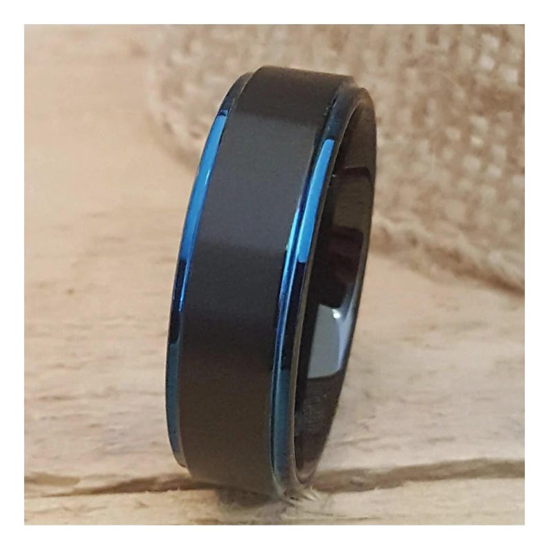 Puede incluir: Un anillo negro y azul con acabado cepillado. El anillo tiene una fina banda azul alrededor del borde.