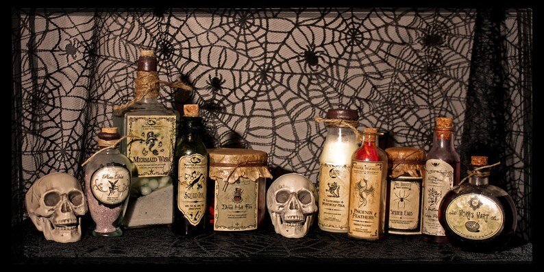 May include: A collection of eight glass bottles with cork stoppers and labels. The bottles are filled with various liquids and have labels with names like "Mermaid Wish", "Phoenix Feathers", and "The Very Last Drop". The bottles are arranged on a black surface with a spiderweb pattern background. Two white skull figurines are in front of the bottles.
