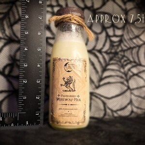 May include: A glass bottle with a brown label and a white liquid inside. The label has a black and white illustration of a werewolf and the text "Pasteurized Werewolf Milk". The bottle is approximately 7.5 inches tall.