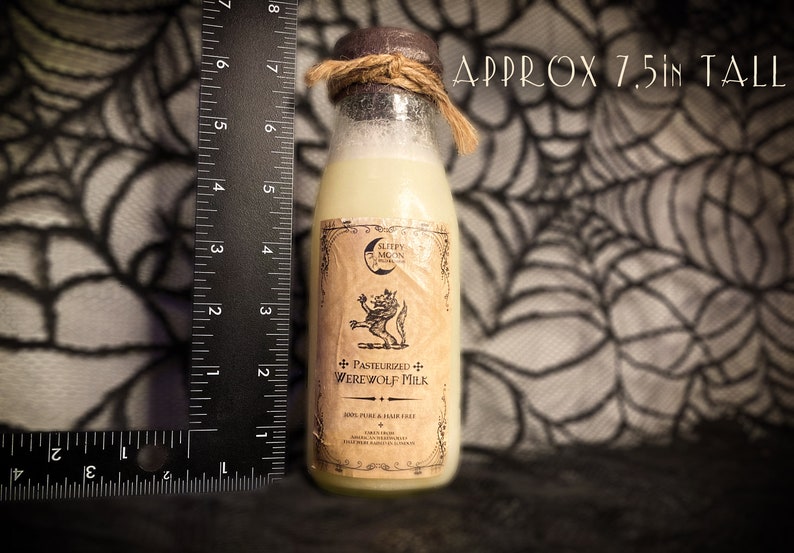 May include: A glass bottle with a brown label and a white liquid inside. The label has a black and white illustration of a werewolf and the text "Pasteurized Werewolf Milk". The bottle is approximately 7.5 inches tall.