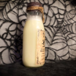 May include: A glass bottle with a white liquid inside and a brown label with a black and white illustration of a creature and text that reads "+ Potion of Wederwart". The bottle is sitting on a black and white patterned surface.