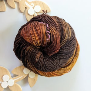 Peut inclure: Une pelote de laine dans des tons de brun, orange et jaune. La laine est enroulée en boule et est prête à être utilisée pour le tricot ou le crochet.