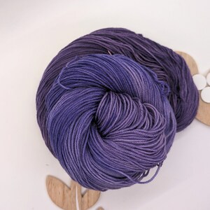May include: A skein of purple yarn with a gradient of colour from dark to light. The yarn is soft and fluffy, and it is perfect for knitting or crocheting.