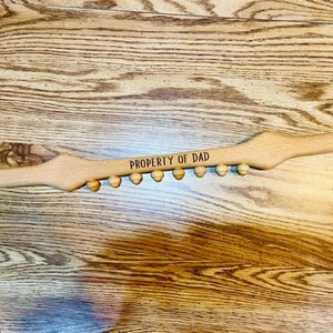May include: A wooden back scratcher with a row of rounded knobs and the text "PROPERTY OF DAD" engraved on the top.