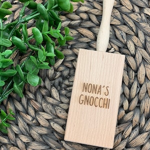 Puede incluir: Prensa de ñoquis de madera con mango. La prensa está grabada con el texto "NONA'S GNOCCHI".