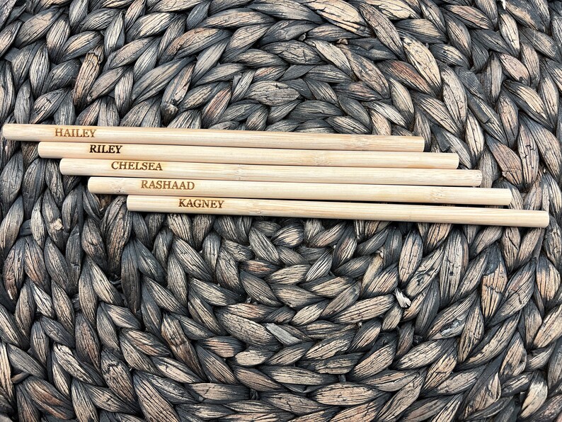 Puede incluir: Cinco palitos de bamb&uacute; natural con nombres grabados: Hailey, Riley, Chelsea, Rashaad y Kagney. Los palitos est&aacute;n dispuestos sobre una superficie de mimbre marr&oacute;n tejido.