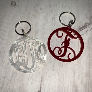 May include: Two keychains with a circle design. One keychain is white with a monogram and the other is red with a single letter F.