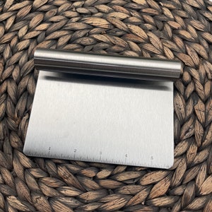 May include: A silver metal pastry scraper with a ruler marked 1 to 5. The scraper has a removable handle.