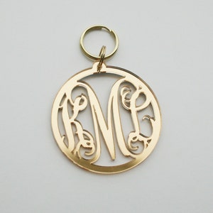 May include: Gold-toned metal keychain with a circular design featuring a monogrammed letter "M" with decorative flourishes.