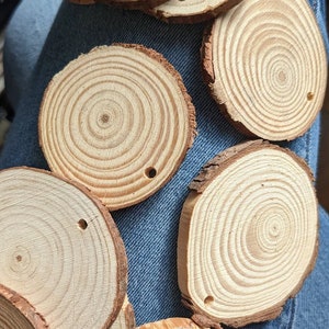 May include: A collection of six natural wood slices, each with a hole drilled in the center. The slices are arranged on a blue denim background.
