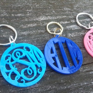 May include: Three keychains with different colored round charms. The charms are made of plastic and have a monogram design. The keychains are silver, gold, and silver.