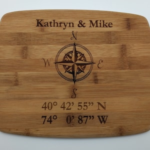 May include: A personalised bamboo chopping board with a compass design and the text "Kathryn & Mike" and coordinates "40° 42' 55" N 74° 0' 87" W".