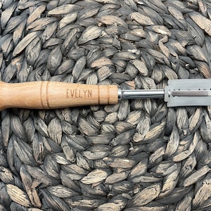 Puede incluir: Un cortador de masa con mango de madera y hoja de metal. El mango está grabado con el nombre "EVELYN".