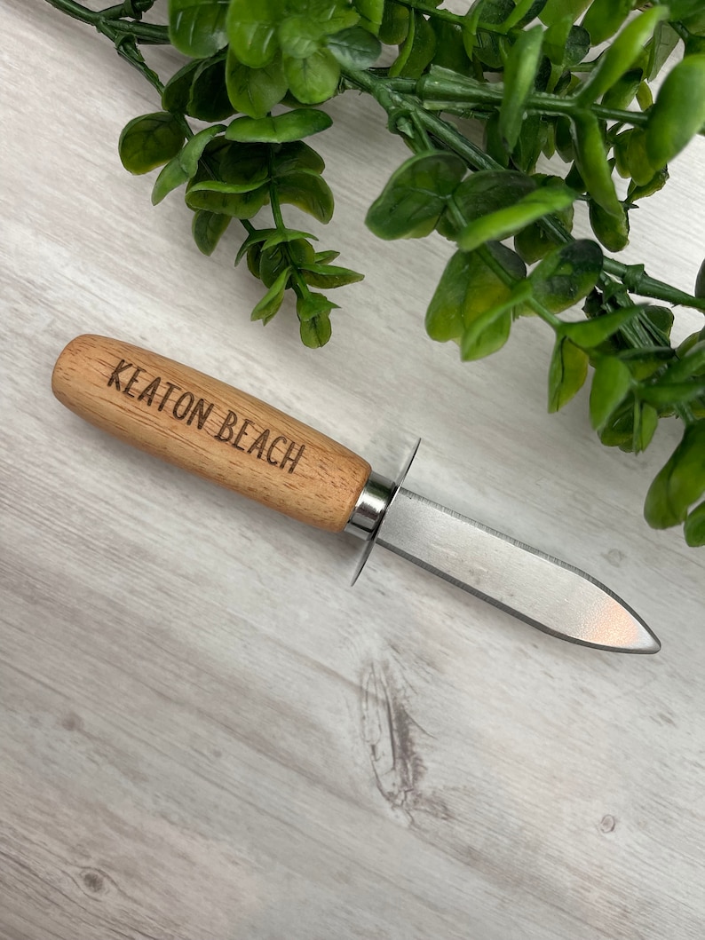 May include: A small oyster knife with a wooden handle and a stainless steel blade. The handle is engraved with the words "Keaton Beach".