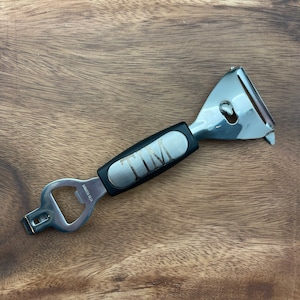 May include: A silver multi-tool with a black handle. The handle has the name "TIM" engraved on it. The tool includes a bottle opener, a peeler, and a small knife.