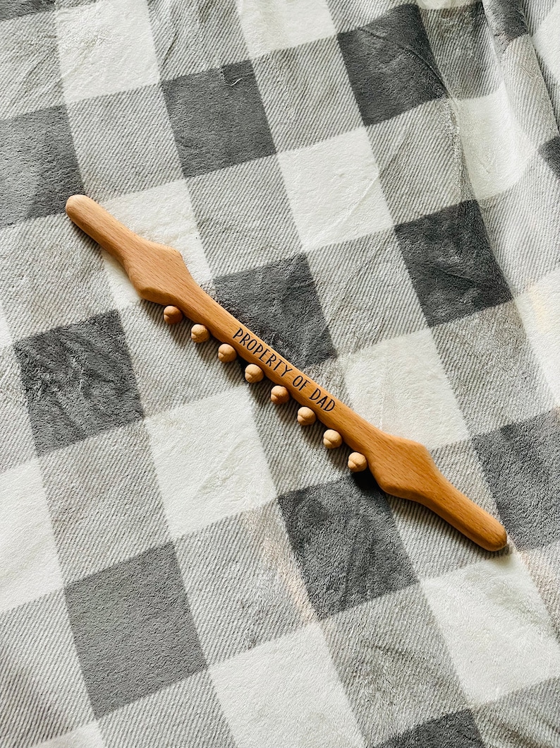 May include: A wooden back scratcher with a handle and rounded knobs. The back scratcher is engraved with the text "PROPERTY OF DAD".