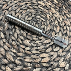 May include: A silver bread knife with a blade and a handle that says "Ready Set Go!" The knife is on a woven brown surface.