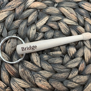 May include: A wooden drumstick keychain with a silver key ring. The drumstick is engraved with the word "Bridge".