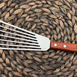 May include: A stainless steel spatula with a wooden handle. The handle has the name "TALLY" engraved on it.