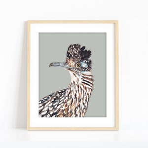 Pu&ograve; includere: Un dipinto ad acquerello di un roadrunner con uno sfondo grigio. L'uccello ha un becco lungo e appuntito, una testa crestata e piume macchiate di marrone e bianco.