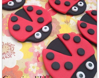 May include: A collection of red and black ladybug-shaped cake toppers with white eyes. The ladybugs have black spots and are made of fondant.