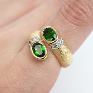 May include: A gold ring with two green oval gemstones and small white gemstones. The ring has a textured band.