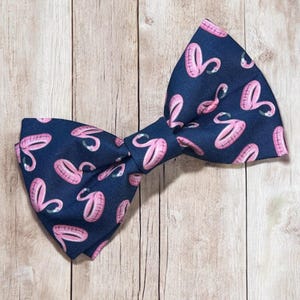 Pode incluir: Uma gravata borboleta azul marinho com um padrão de flamingos rosa. A gravata borboleta é feita de um tecido macio e confortável e é perfeita para adicionar um toque de fantasia a qualquer roupa.