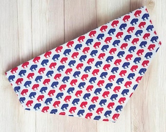 May include: A triangular pet bandana featuring a repeating pattern of small, stylized buffalo silhouettes in alternating red and dark blue colors against a white background, with stitched edges forming a clean, finished border.