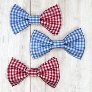 Op de afbeelding: Drie vlinderstrikken met een klassiek vichy-ruitpatroon. Eén vlinderstrik is verdeeld in blauw en rood, één is effen blauw en één is effen rood. Elke vlinderstrik heeft een centrale stoffen knoop en een gestructureerde, geplooide vorm met puntige uiteinden.