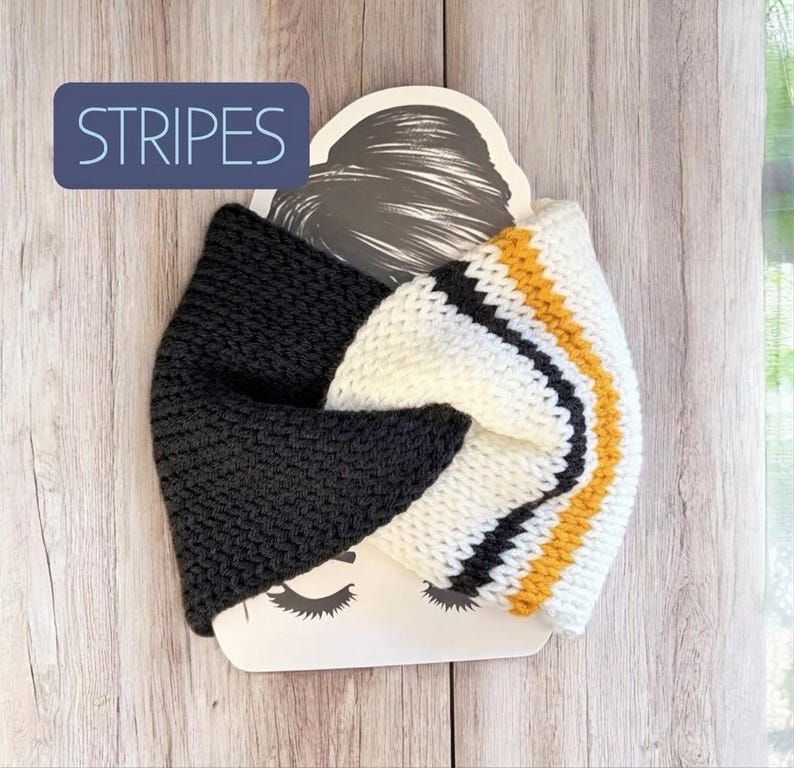 May include: A knitted headband featuring a twisted front design. One side is solid charcoal grey, while the other side displays white, black, and mustard yellow stripes. The headband is displayed on a card with the word STRIPES printed in white.