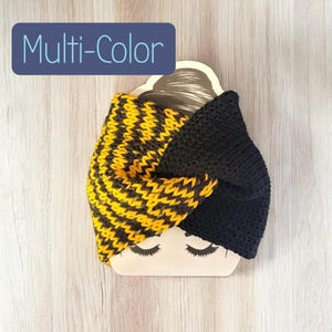May include: A knitted headband featuring a twisted design with one half in solid black and the other half in a yellow and black chevron pattern. The item is displayed on a beige card with a printed face illustration and the text Multi-Color.