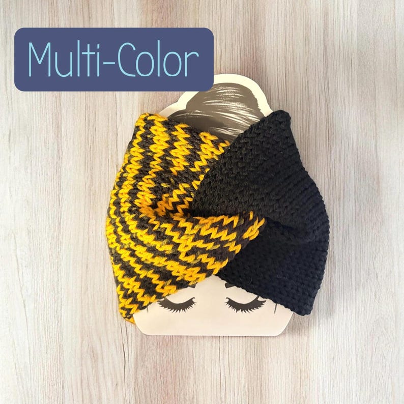 May include: A knitted headband featuring a twisted design with one half in solid black and the other half in a yellow and black chevron pattern. The item is displayed on a beige card with a printed face illustration and the text Multi-Color.