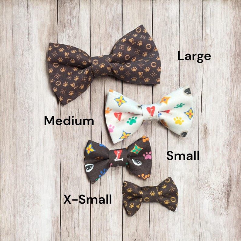 May include: Four bow ties in varying sizes labeled Large, Medium, Small, and X-Small. The Large and X-Small ties are dark brown with gold paw print patterns. The Medium tie is white with colorful paw prints and hearts. The Small tie is dark brown.