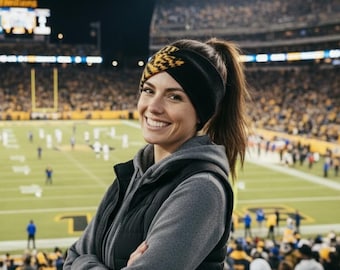 May include: A black and yellow patterned headband worn on the head, paired with a grey hooded sweatshirt and a black quilted vest. The headband features a twisted knot design at the front and is made of a soft, flexible fabric material.