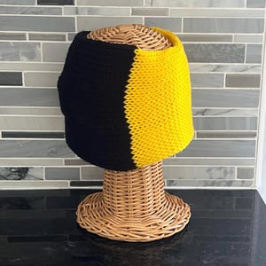 May include: A two-toned knit headband featuring a solid black section on the left and a vibrant yellow section on the right. The accessory is crafted with a consistent ribbed texture throughout, displaying a clear vertical colour split design.