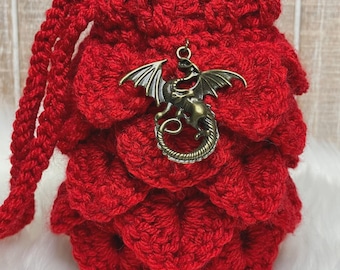 May include: A handmade red crochet drawstring bag with a dragon scale design. The bag features a bronze-colored dragon charm and a braided drawstring. The bag is approximately 6 inches tall and 4 inches wide.