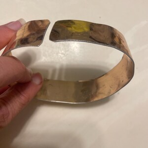 May include: A silver metal bangle bracelet with a gap in the design. The bracelet is open and appears to be made of a single piece of metal.