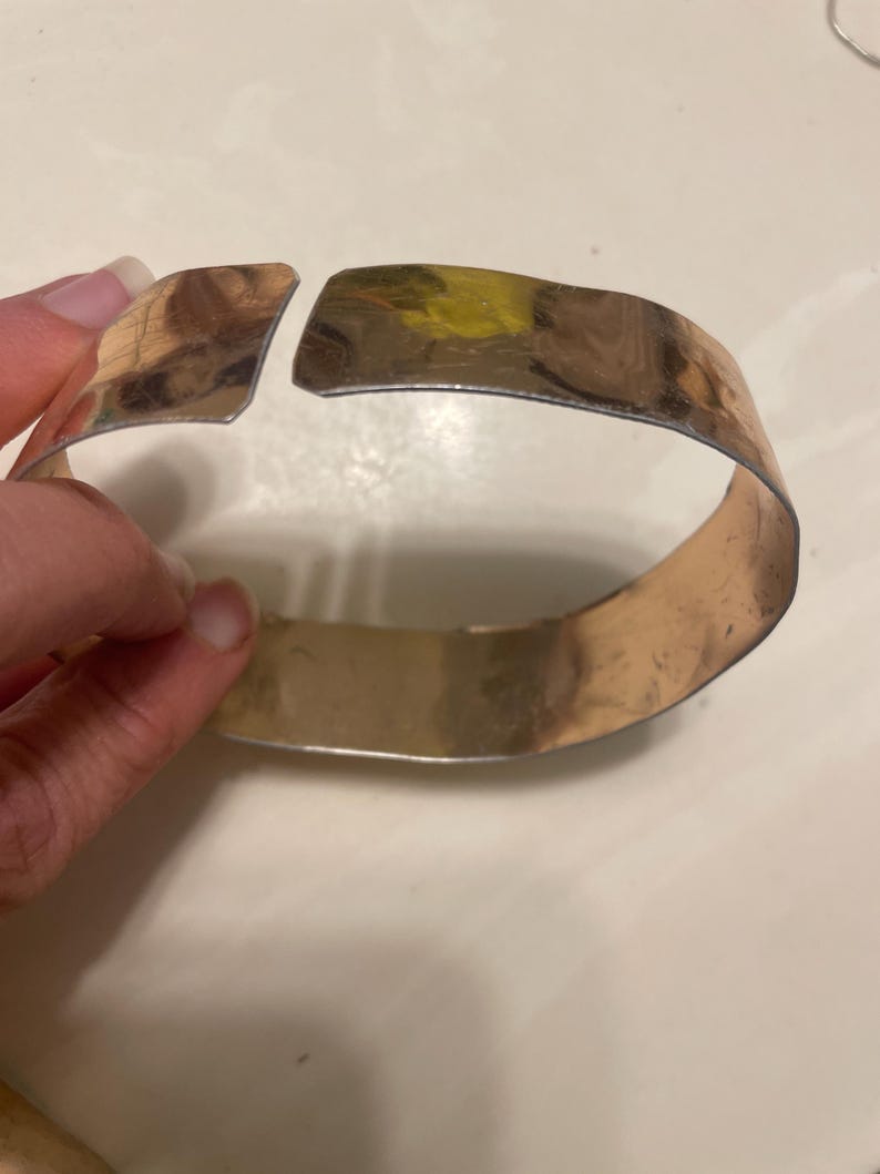 May include: A silver metal bangle bracelet with a gap in the design. The bracelet is open and appears to be made of a single piece of metal.