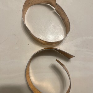 May include: Two gold-colored metal bracelets, one is a complete circle and the other is a partial circle.