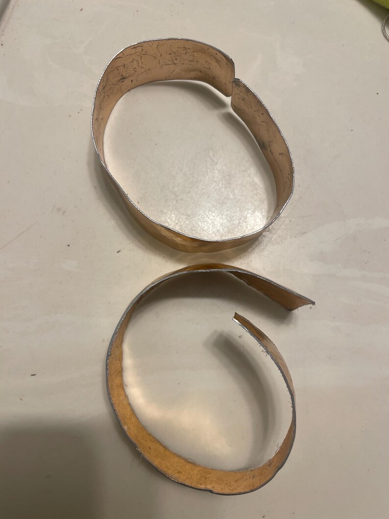 May include: Two gold-colored metal bracelets, one is a complete circle and the other is a partial circle.