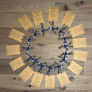 May include: A circular arrangement of twelve paracord keychains, each featuring a blue and white pattern with a white bead, attached to a rectangular tan card. Each card displays the text LA Dodgers, Team Spirit, and We are a great team because of you.