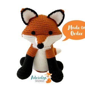 May include: A crocheted fox plush toy with orange and white fur, black eyes, and black legs. The toy is sitting on a white background with a speech bubble that says "Made to Order".