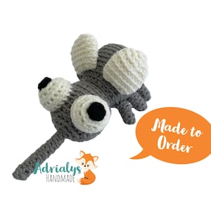 May include: A handmade crochet elephant toy in gray and white. The elephant has large, round eyes with black pupils, large white ears, and a trunk. The text "Made to Order" is in an orange speech bubble. The shop logo is also visible.