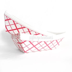 May include: A stack of white paper food boats with a pink and white checkered pattern. The boats are folded and ready to be used.