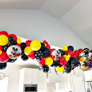 May include: A Mickey Mouse themed balloon garland with red, yellow, black, and white balloons. The garland features Mickey Mouse character balloons and polka dot balloons.