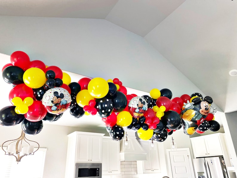 May include: A Mickey Mouse themed balloon garland with red, yellow, black, and white balloons. The garland features Mickey Mouse character balloons and polka dot balloons.
