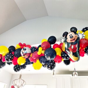 May include: A Mickey Mouse themed balloon garland with red, yellow, and black balloons. The garland includes a large Mickey Mouse balloon and smaller balloons with black polka dots.