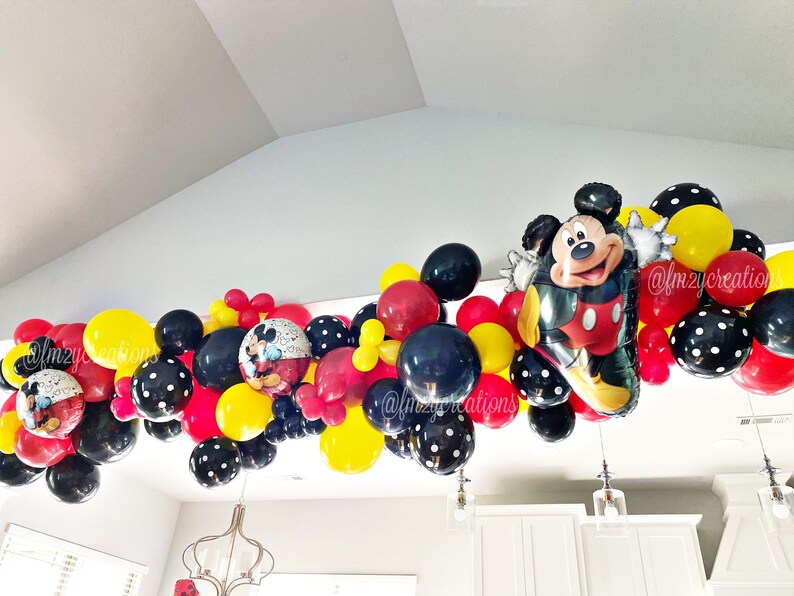 May include: A Mickey Mouse themed balloon garland with red, yellow, and black balloons. The garland includes a large Mickey Mouse balloon and smaller balloons with black polka dots.