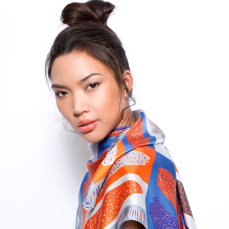 May include: A woman with dark hair styled in a bun wears a colourful silk scarf with a geometric pattern in shades of blue, orange, and white.