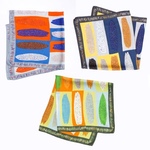 May include: Three colourful silk scarves with abstract patterns of brushstrokes and dots. The scarves are in shades of orange, blue, green, yellow, and white. The scarves have a fringed edge.